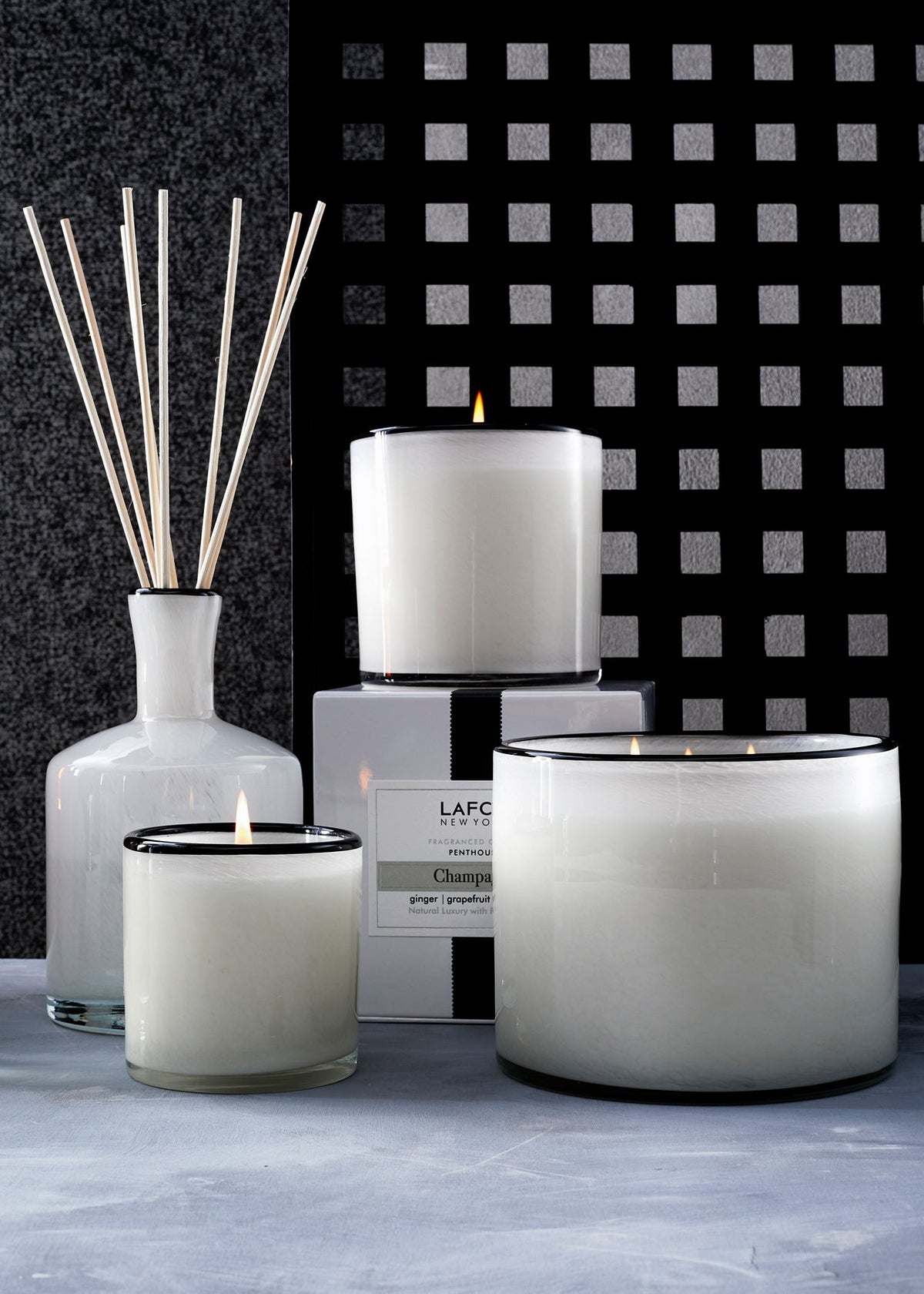 Front view of LAFCO Champagne candles and diffuser showcasing white frosted glass vessels with black rims and lit wicks