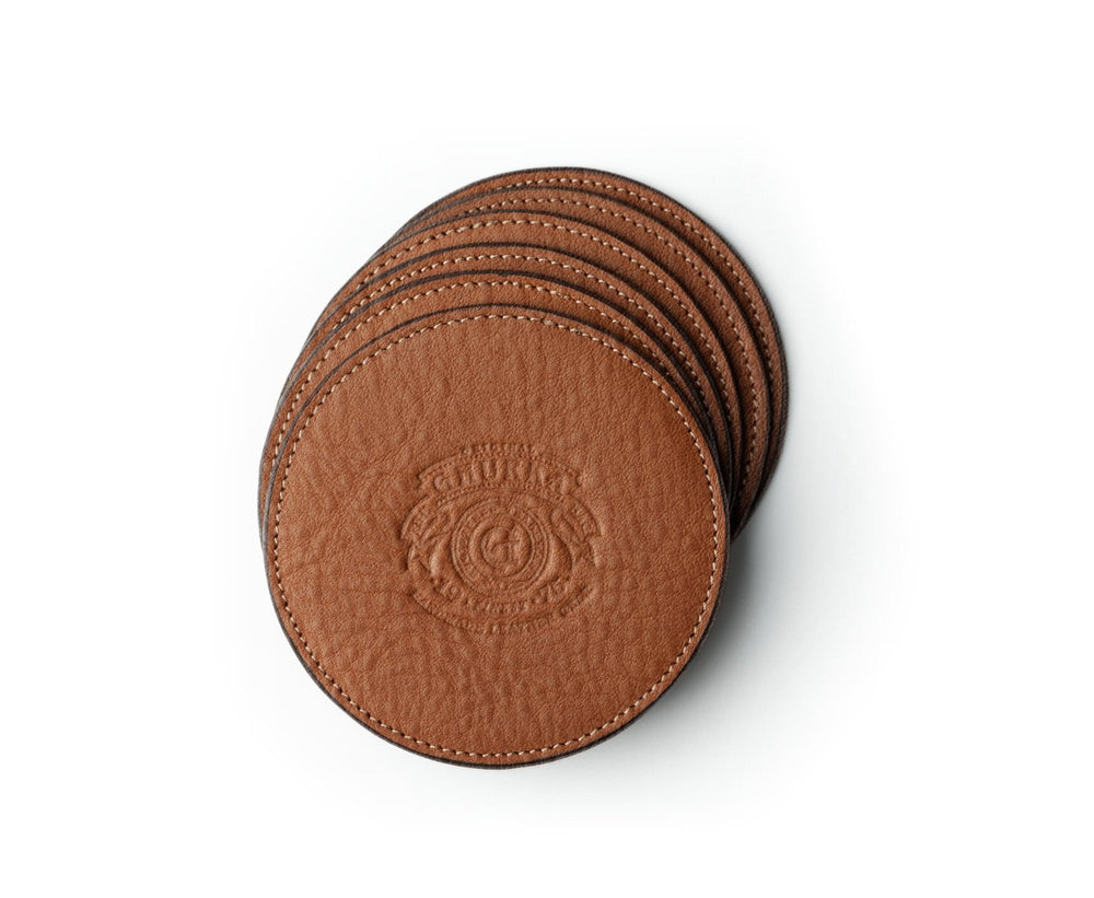 Top view of leather coaster set of six in vintage chestnut showcasing embossed crest and stitched edges on white background