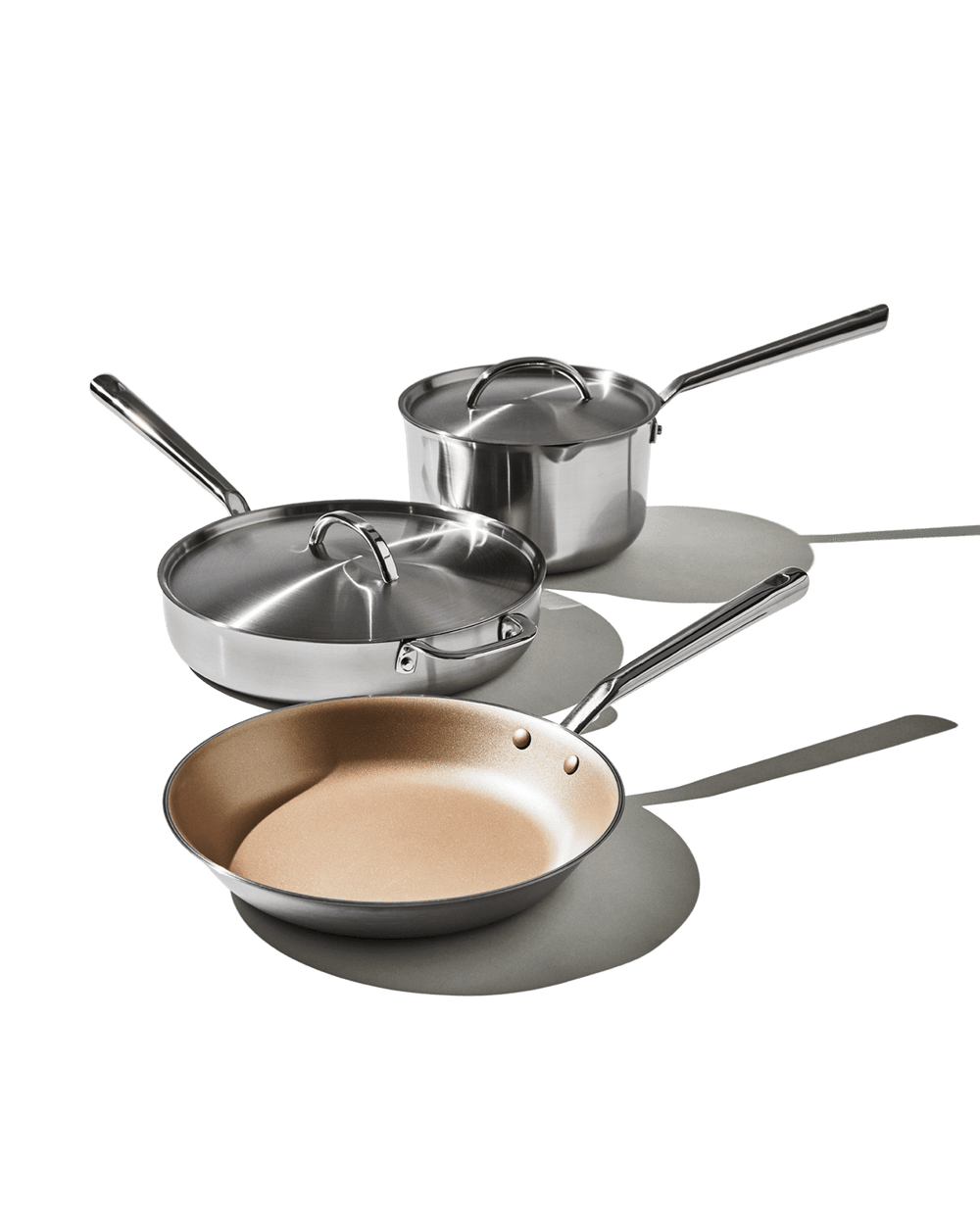 Three-quarter view of The Copper Set showing copper-colored nonstick interior, stainless-steel exteriors, lids and long handles on white background
