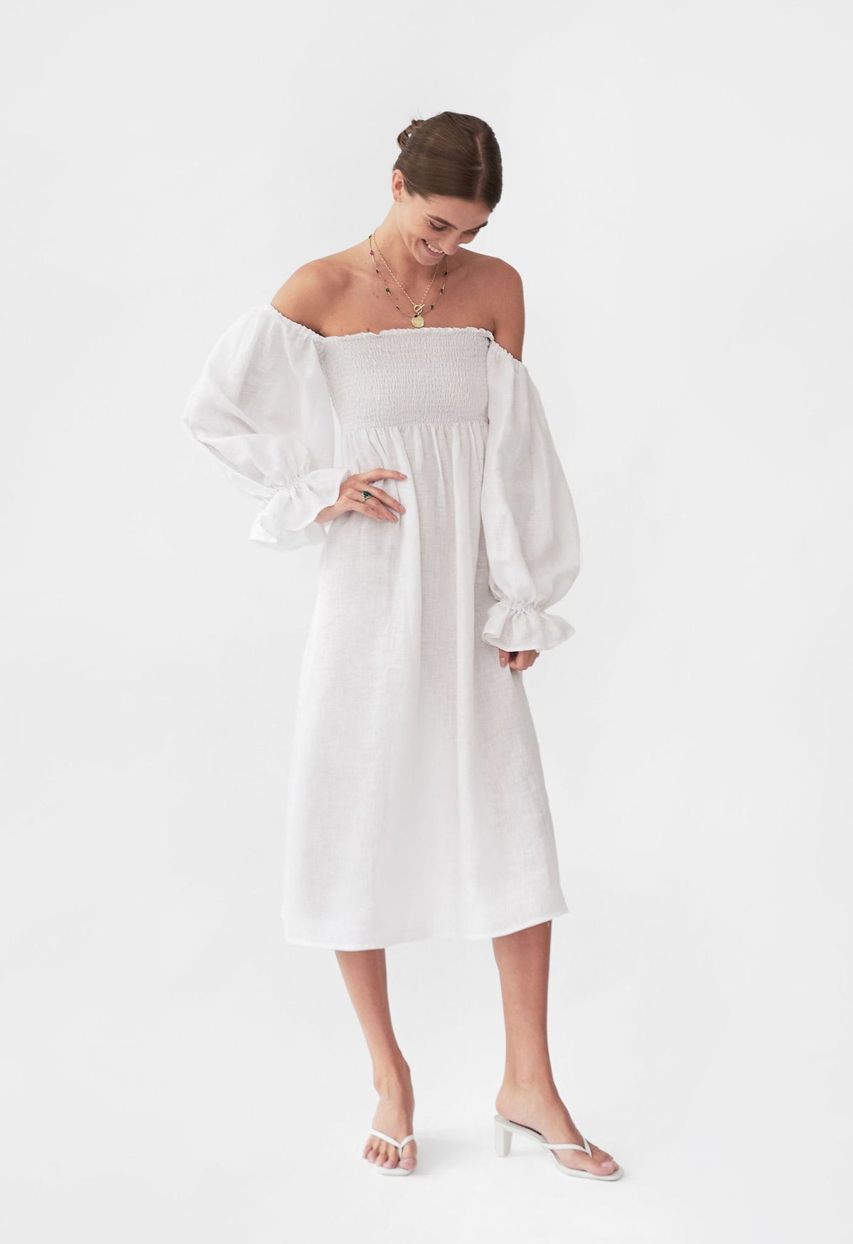 Front view of Atlanta Linen Dress in White showcasing its smocked waistline and off shoulder sleeves on a plain background