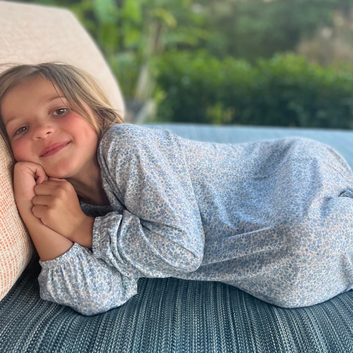 Side view of Girls Slate Floral Pima Dress showing floral print and three-quarter sleeves on a girl reclining in a cushioned chair