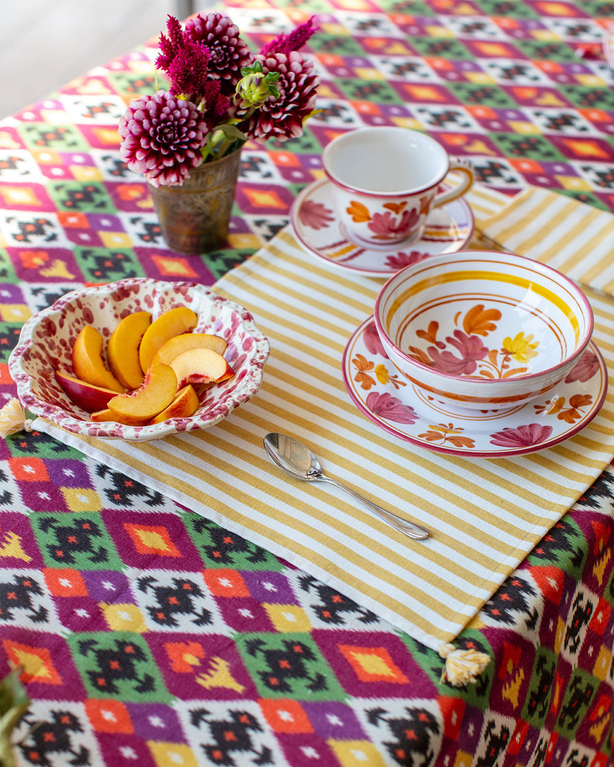 Burgundy Blossom bowl holding sliced peaches on a colorful dining table with flowers and patterned dishware