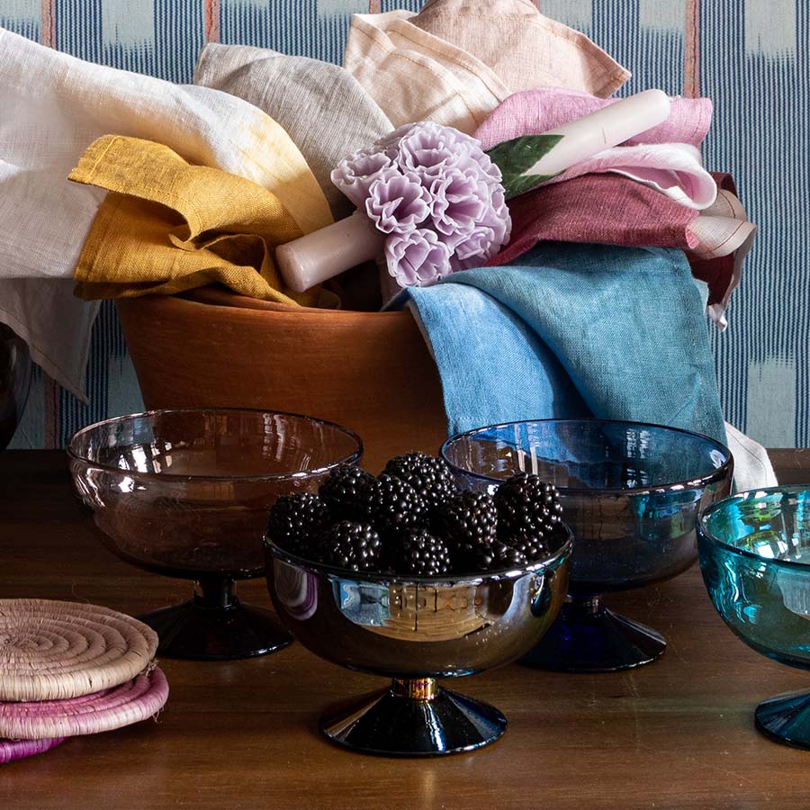 Front view of smoke glass footed bowl showing iridescent finish and pedestal base on wooden table with linens