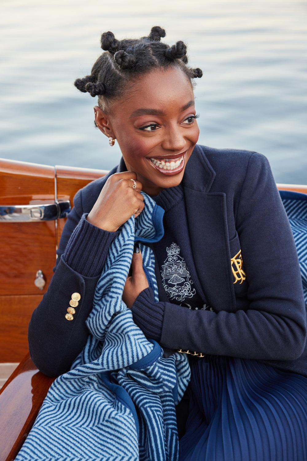 Woman holding Harborview Herringbone Navy blanket, smiling on a wooden boat with calm water in the background