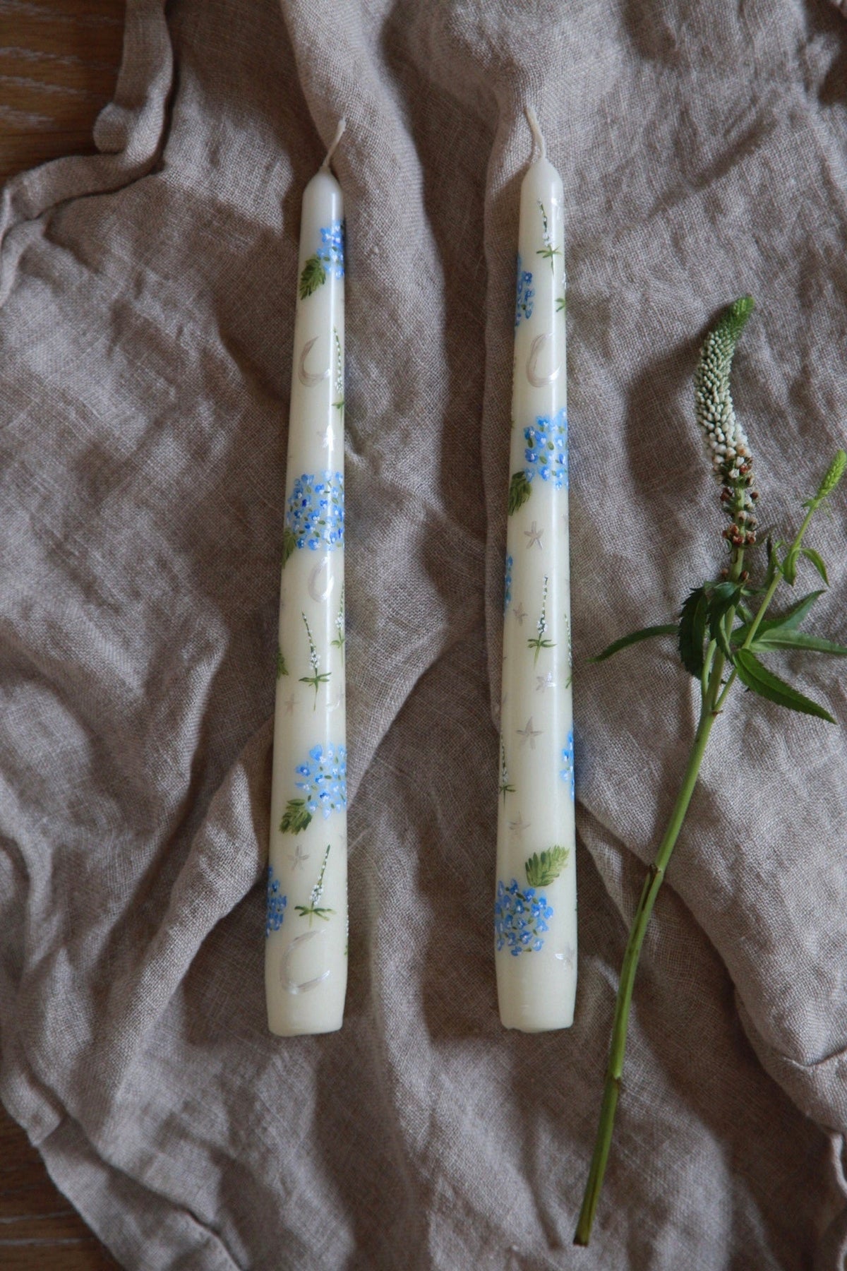 Top view of Ivory Evening Hydrangeas candles, set of two, showcasing blue hydrangeas on off-white wax against linen