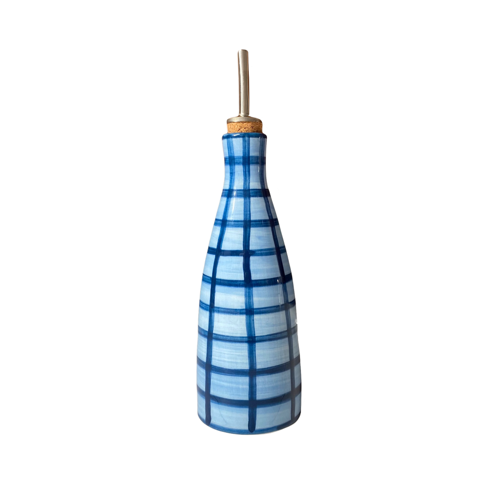 Front view of Oily Baby Gingham oil dispenser, blue hand-painted gingham ceramic body with cork stopper and metal pour spout on white background