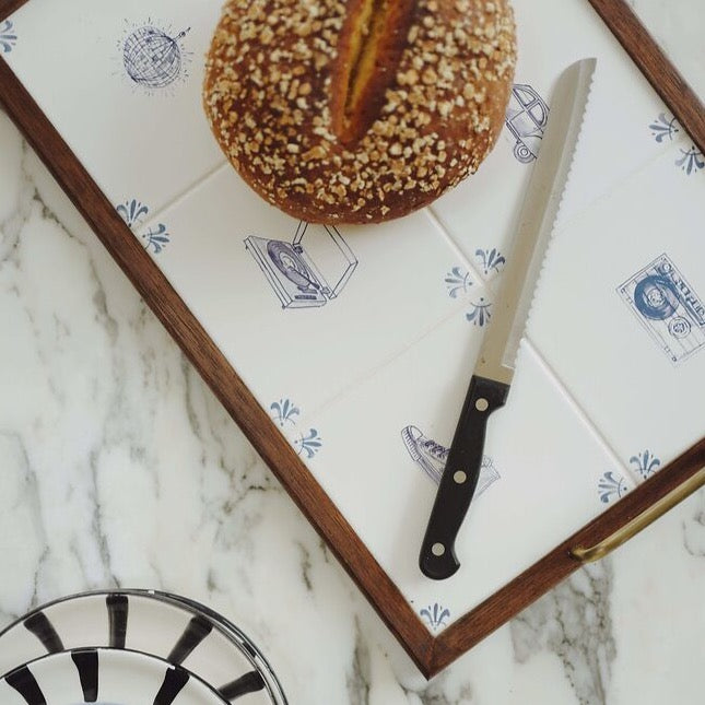 Top-down view of Retro Tile Tray showcasing tiled white surface with blue retro illustrations, walnut frame and brass handle on marble countertop