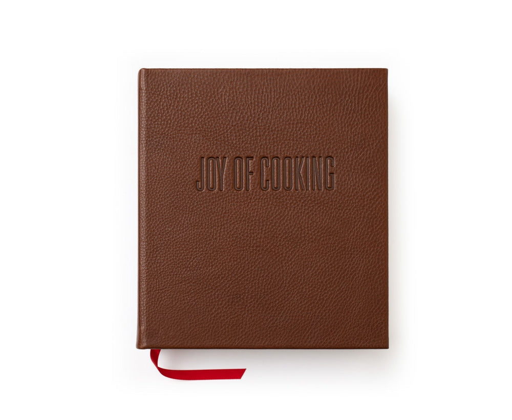 Top-down view of Joy of Cooking hardcover book in vintage chestnut leather showcasing embossed cover title and red ribbon bookmark on white background