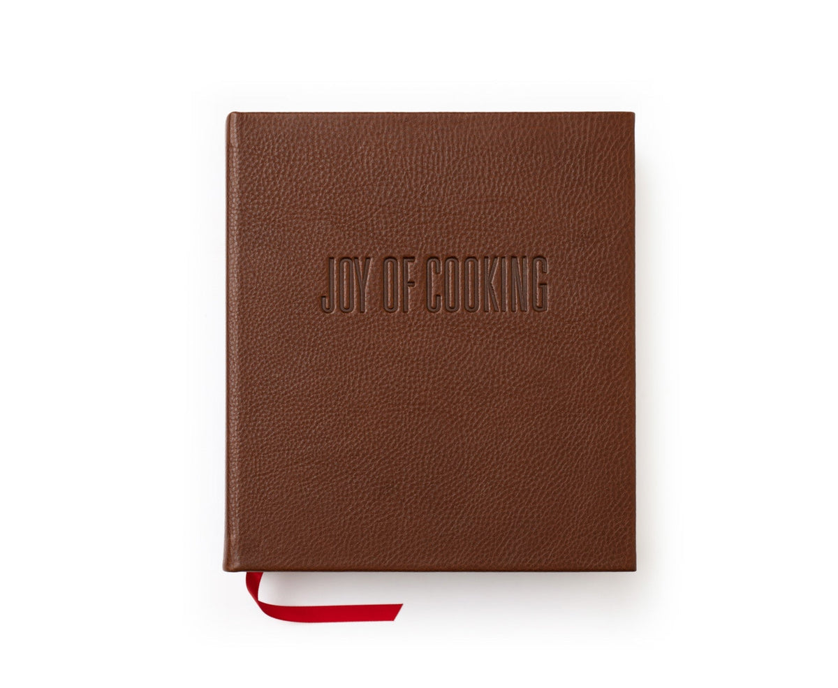Top-down view of Joy of Cooking hardcover book in vintage chestnut leather showcasing embossed cover title and red ribbon bookmark on white background