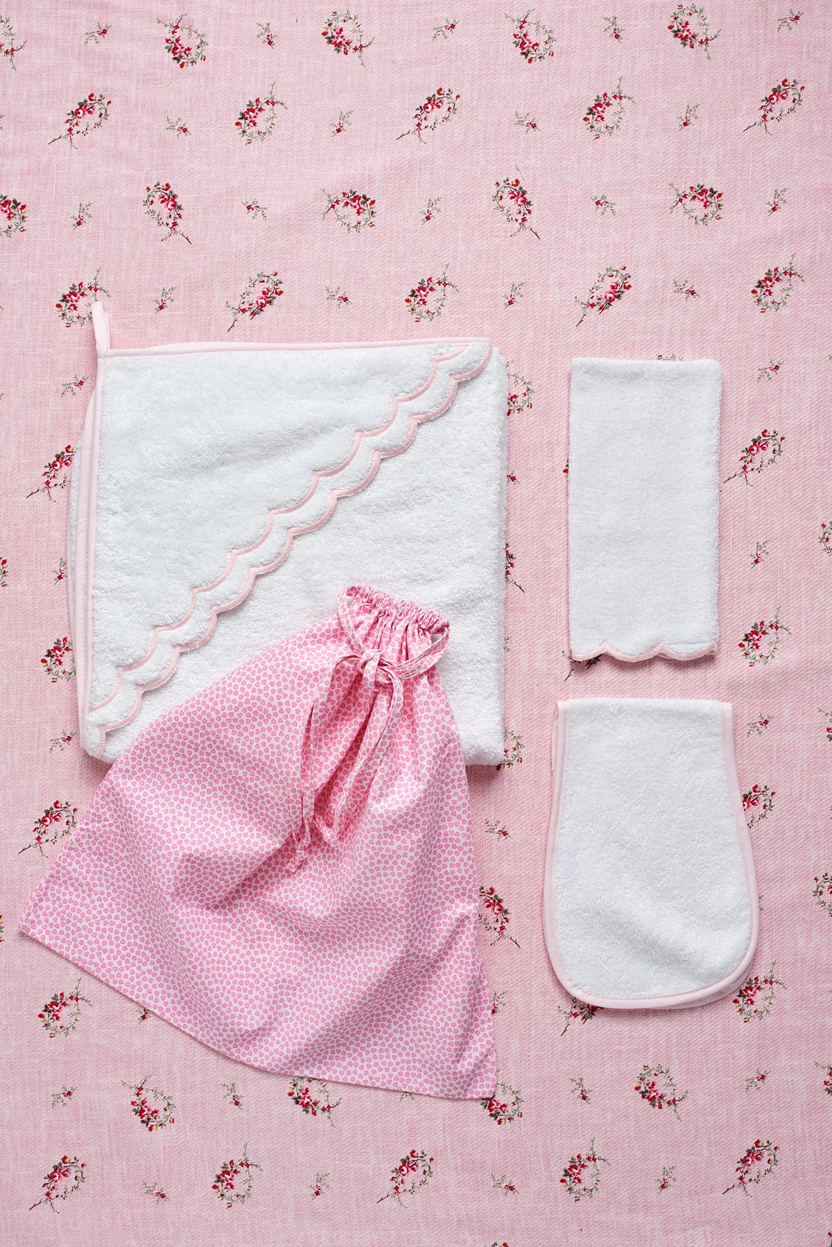 Top view of Loulou Bath Set showcasing white towels and a pink drawstring bag on a floral pink background