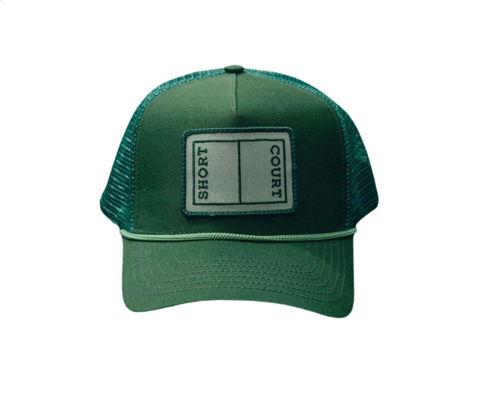 Front view of Short Court Trucker Hat showcasing embroidered ‘SHORT COURT’ patch, braided trim, mesh back, and snap-adjuster on dark background