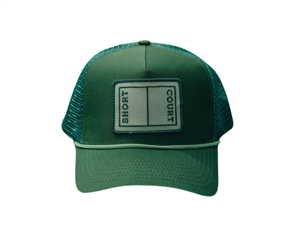 Front view of Short Court Trucker Hat showcasing embroidered ‘SHORT COURT’ patch, braided trim, mesh back, and snap-adjuster on dark background