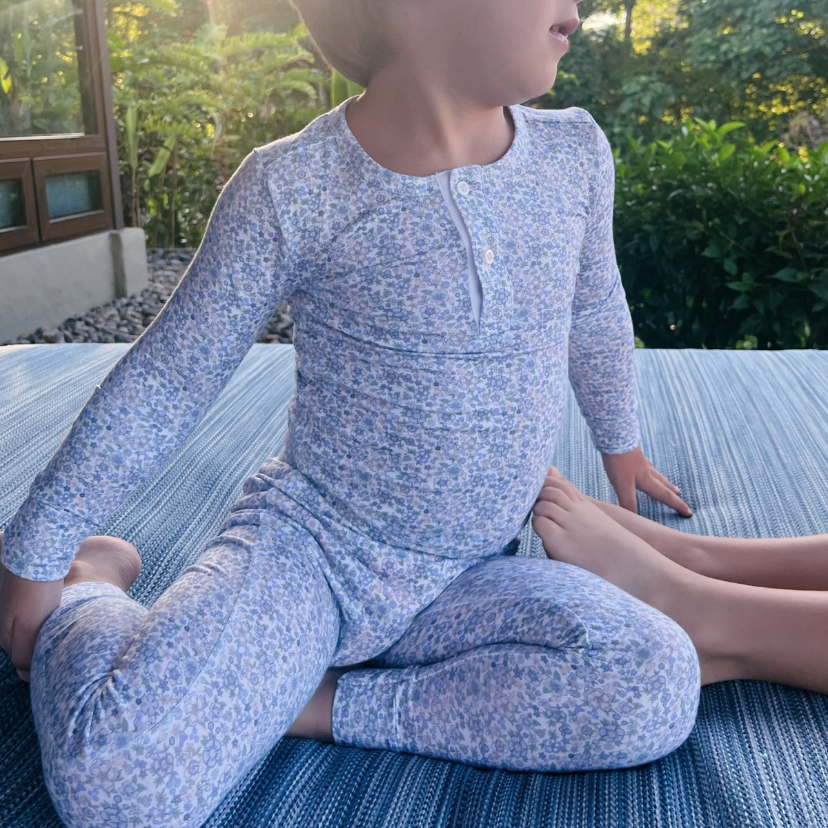 Front view of Unisex Slate Floral Pima Pajama Set showcasing floral print and button front placket with child seated outdoors