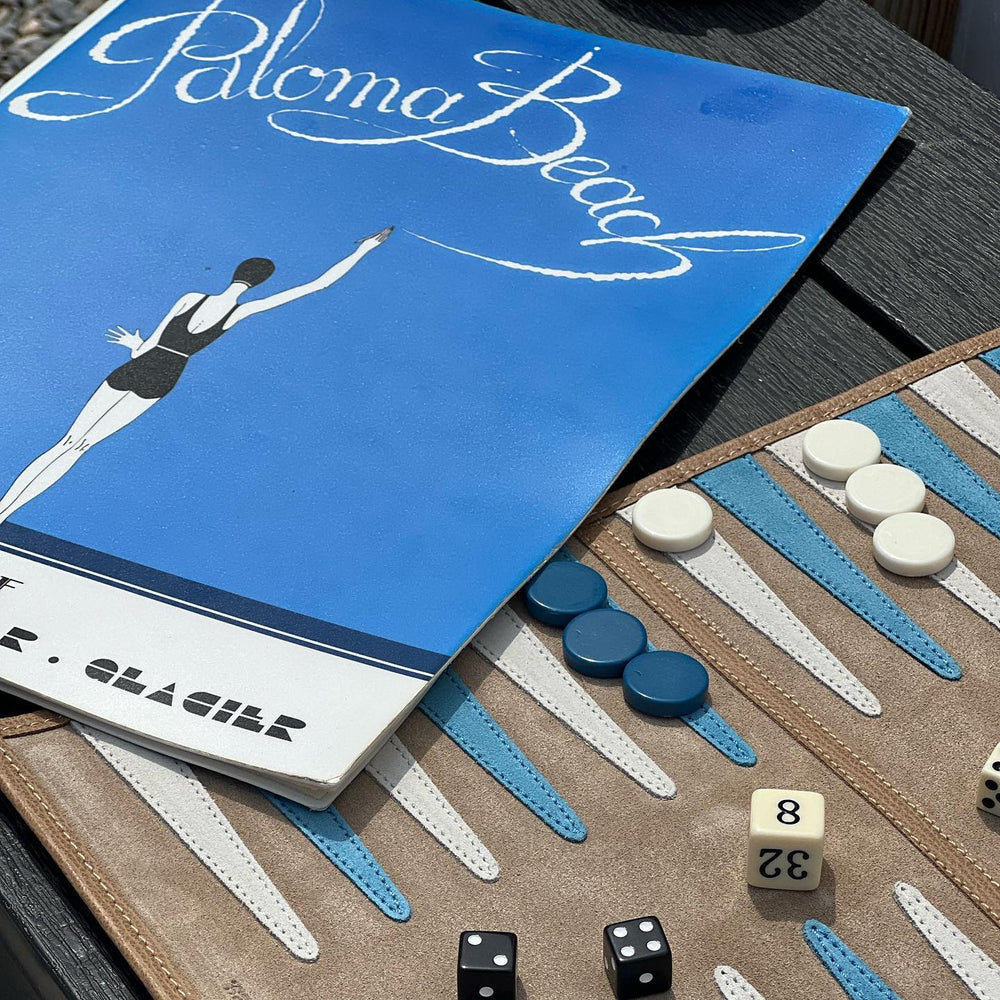 Angled view of St Barth backgammon board showing suede field, blue and white points, dice and chips, and Paloma Beach cover
