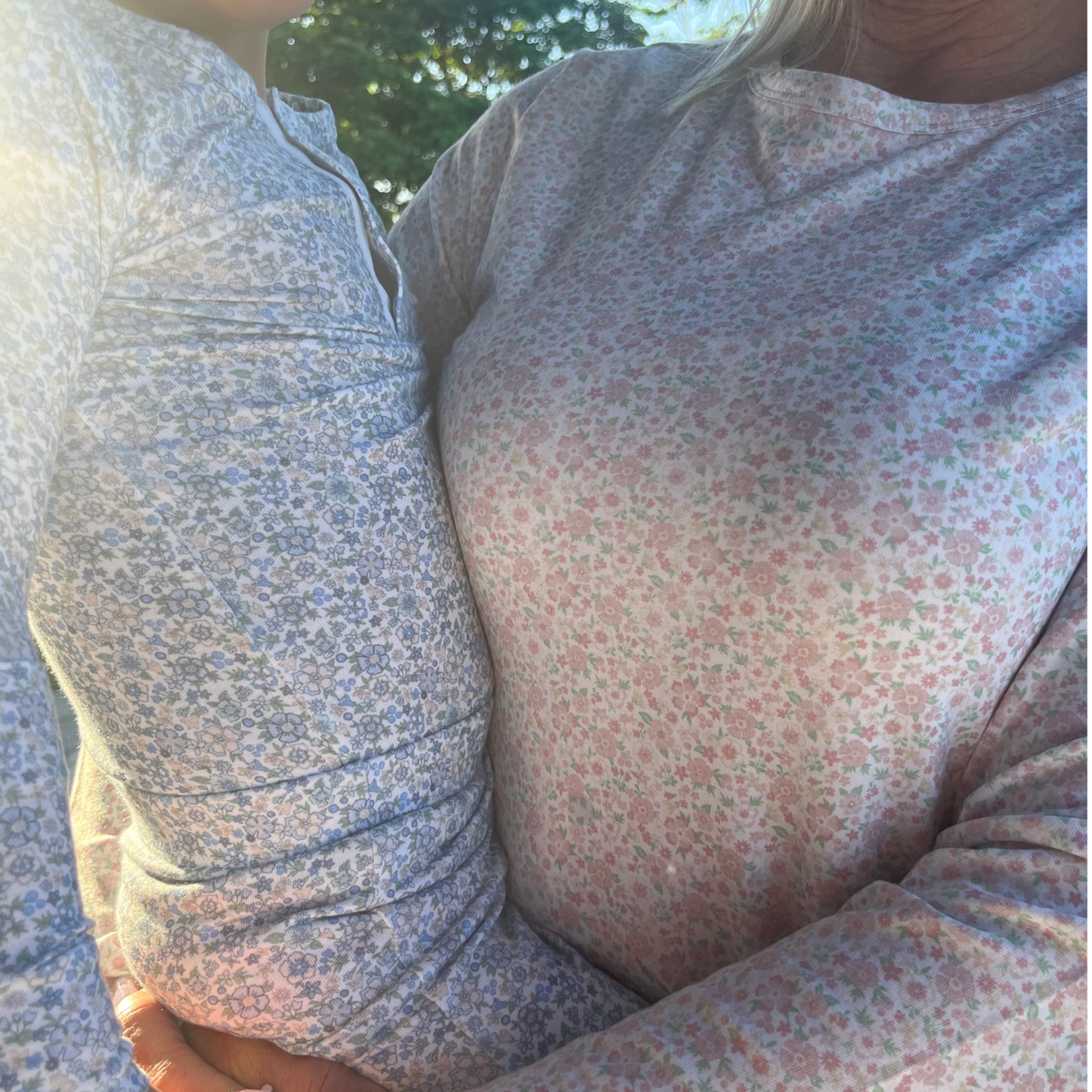 Close-up of an adult and child embracing outdoors wearing antique floral Pima pajama tops with soft sunlit background