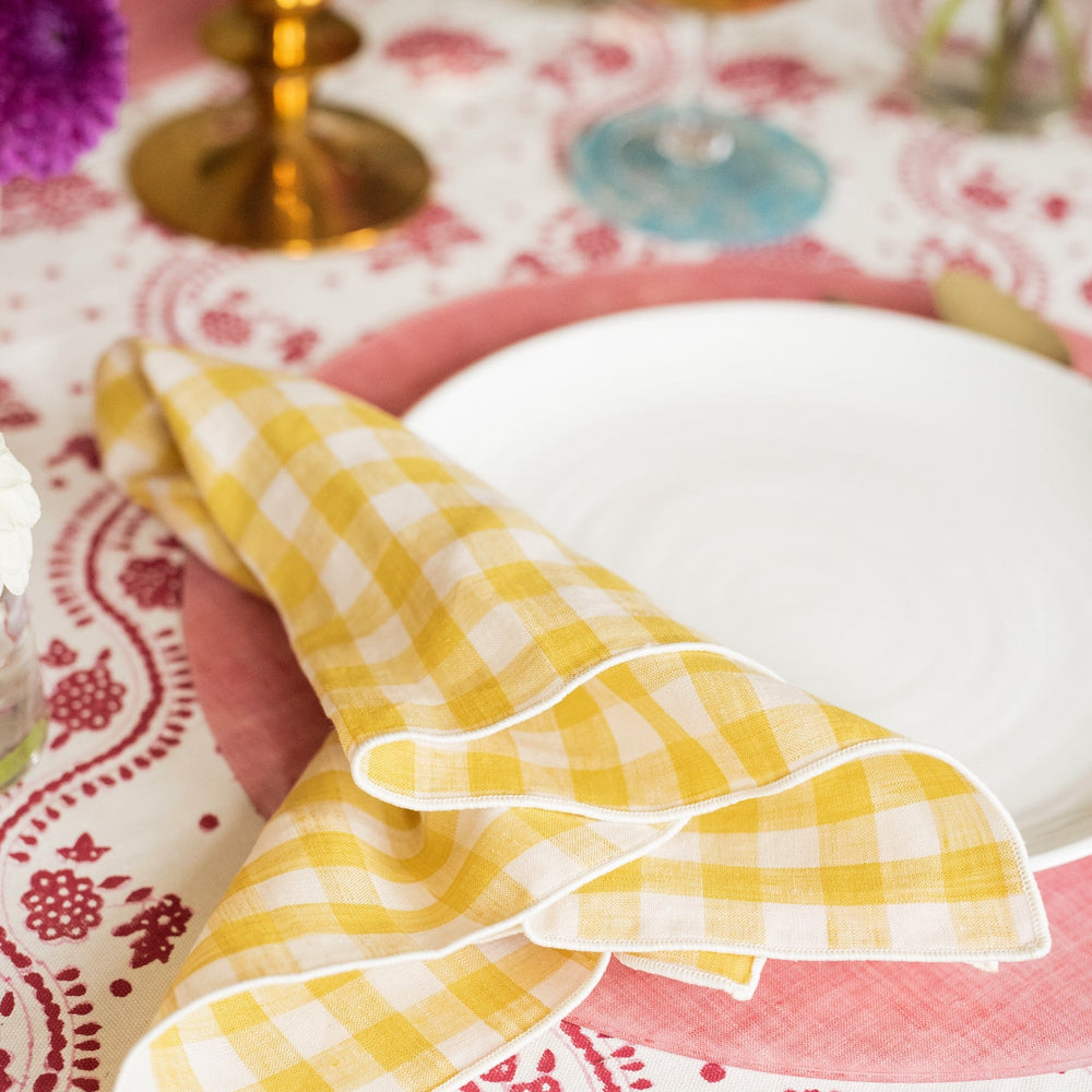 Close-up of Wadsworth Goldenrod Gingham Napkin Set folded on a white plate and pink charger showing yellow gingham linen on a patterned tablecloth