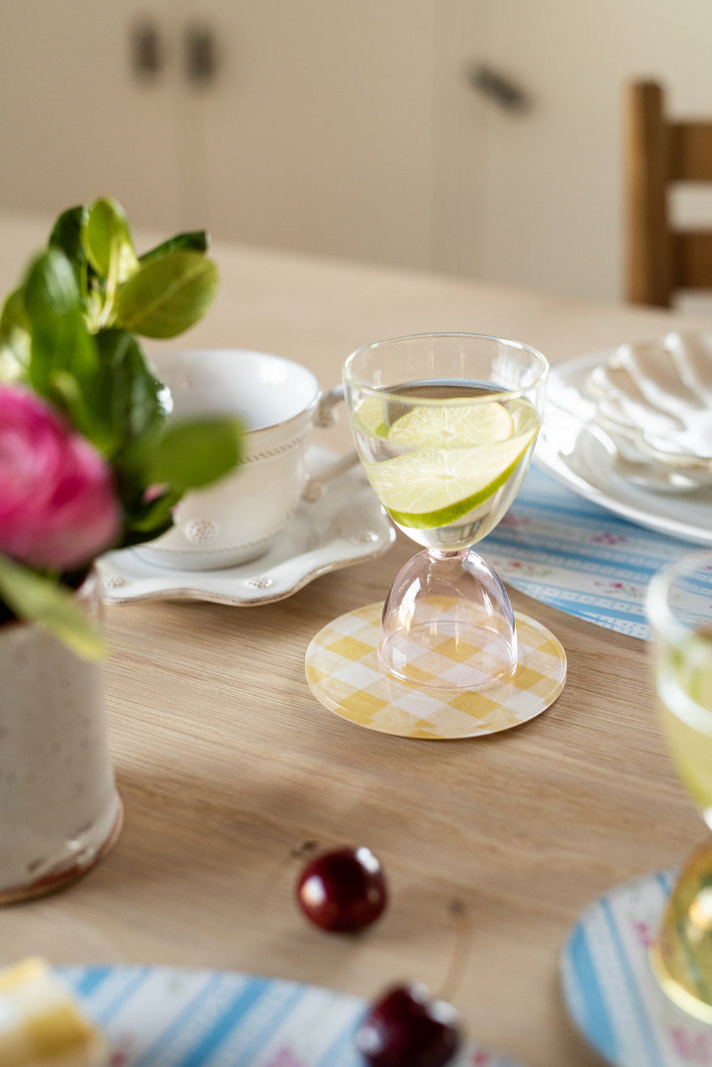 Close-up of Wadsworth Goldenrod Gingham coaster showcasing yellow gingham pattern under a stemmed glass on a wood tabletop