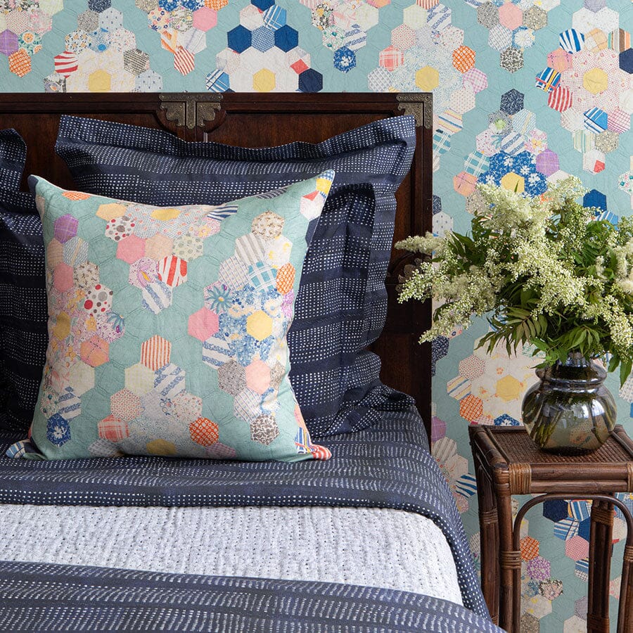 Teal Diamond Quilt Pillow styled on bed with navy dotted shams, wooden headboard, hexagon-print teal wallpaper, and a vase of white flowers on a side table