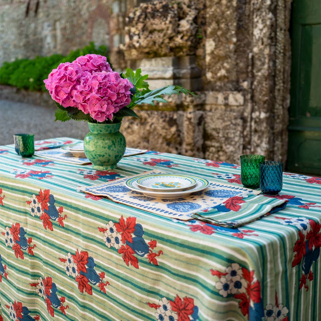 Front view of green vase showcasing hand painted speckled glaze and undulating rim on a patterned tablecloth