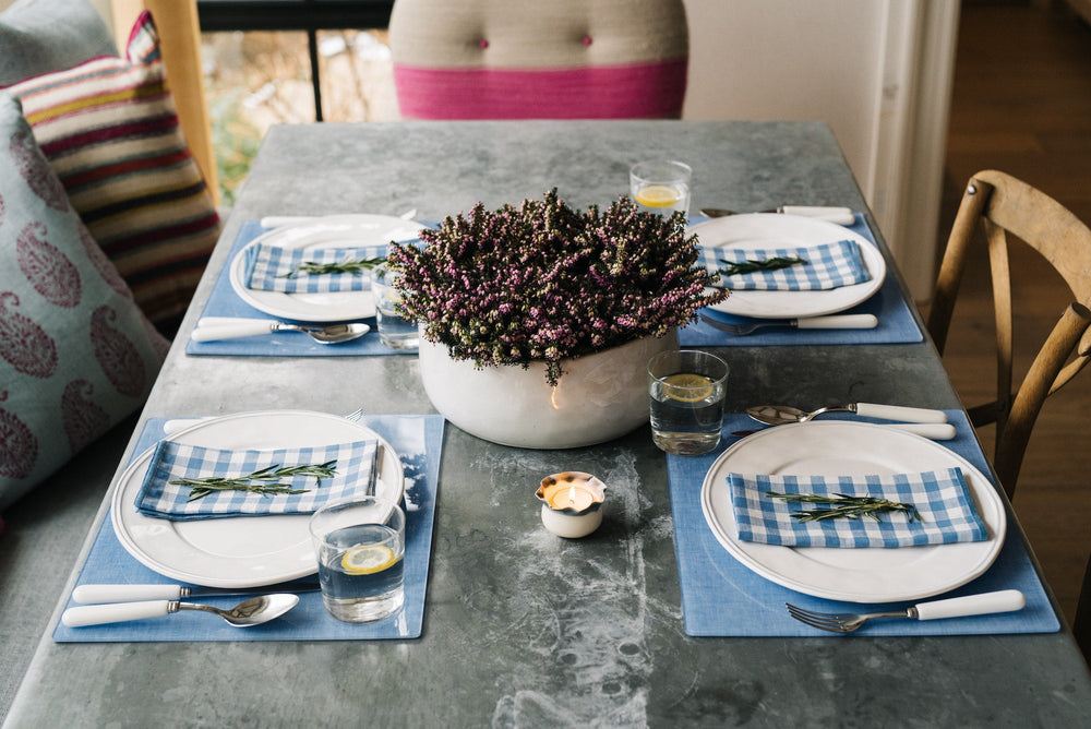Dining table set with Campbell Blue Chambray placemats, white plates, blue gingham napkins, and potted centerpiece