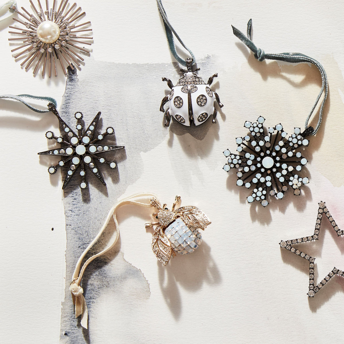 Overhead view of Deco Snowflake Hanging Ornament in Hematite and Opal showcasing silver tones and crystal stones among holiday ornaments